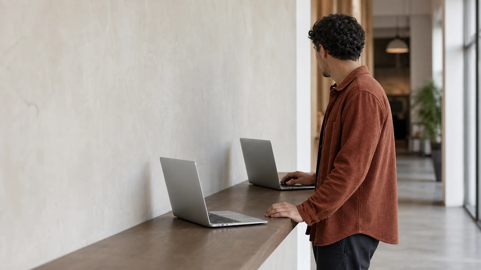 stablecoin shopping online: A person in a rust shirt stands with one hand on a laptop beside a second open laptop on a wooden counter.