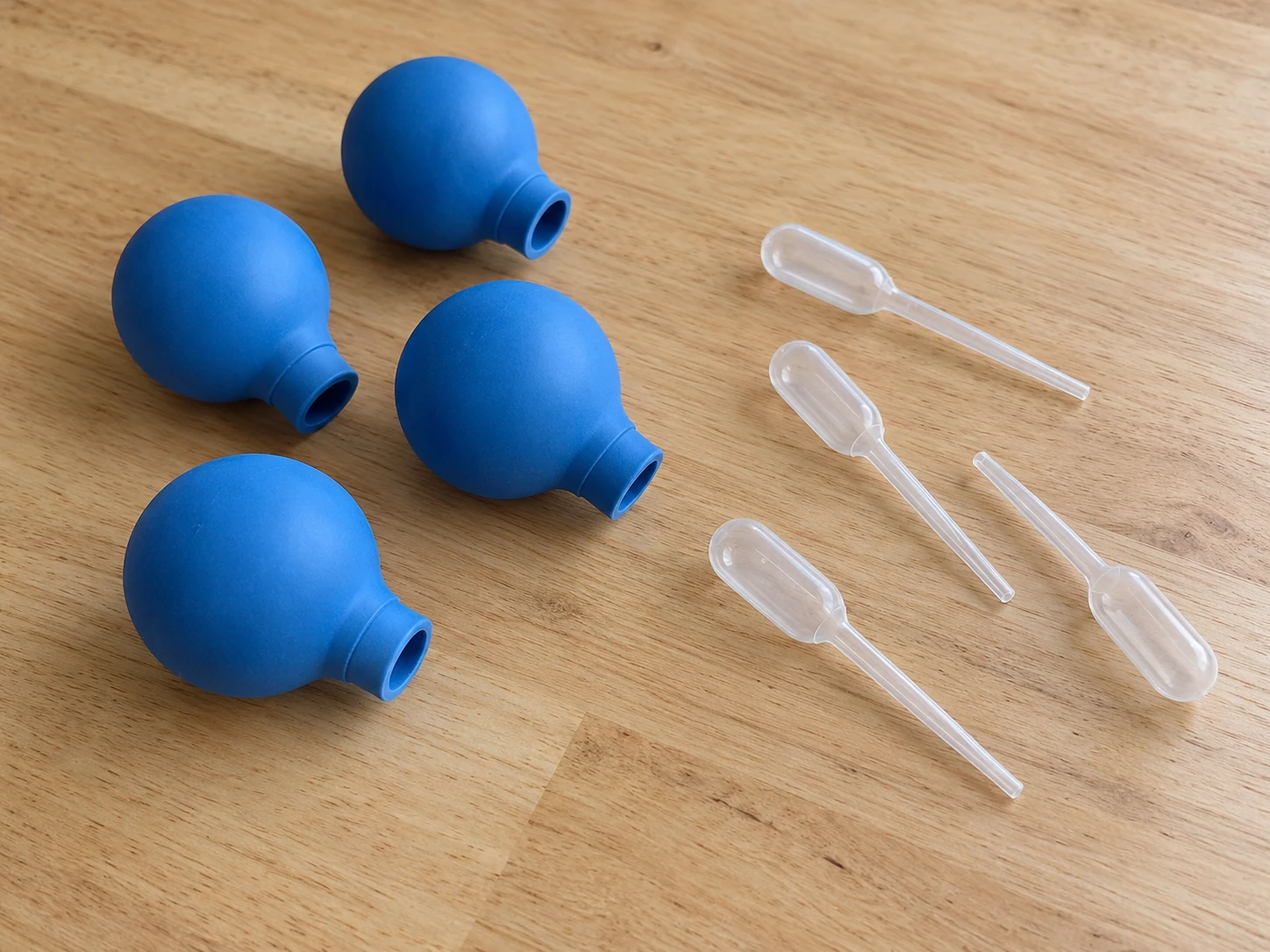 Pipette bulb compatibility concept with separate generic blue bulbs and clear whole droppers resting on a plain table.