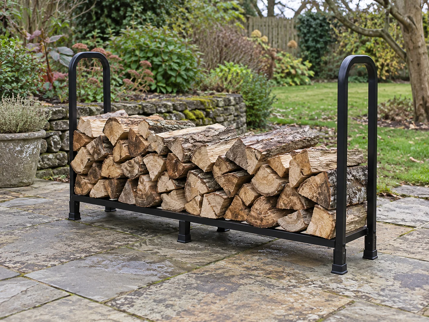 Household firewood routine concept with a whole generic black rack holding a modest stack of split logs on a stone garden patio.