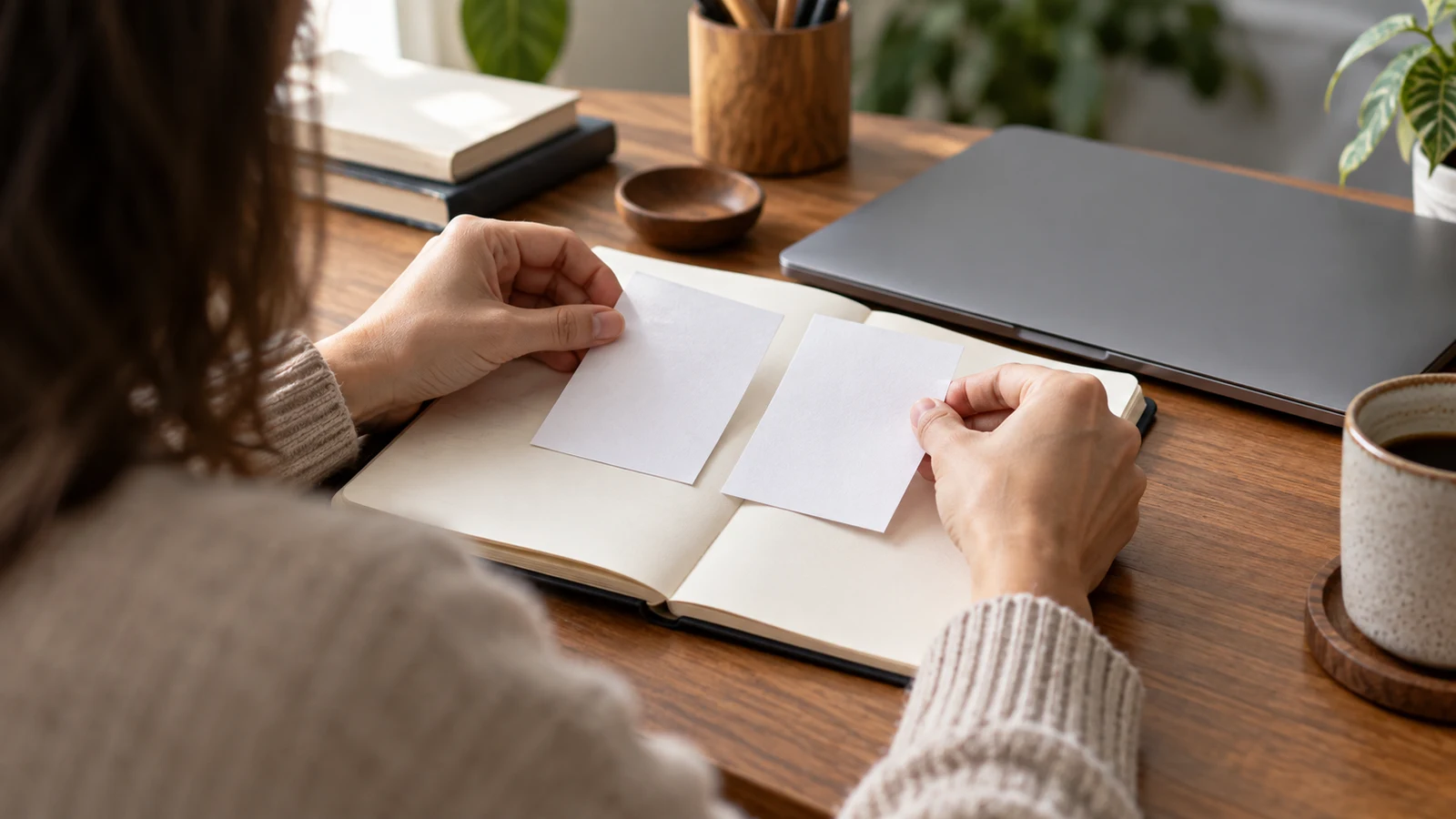 spreadsheet duplicate records: A person holds two blank paper cards side by side on an open notebook.