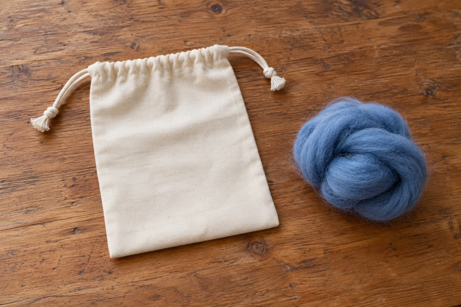 Needle felting on canvas concept with a whole plain canvas pouch and loose wool on a table.